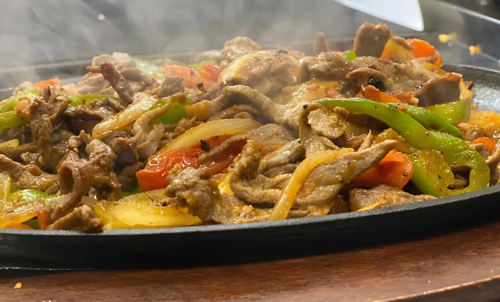 Steak fajitas sizzling on a cast-iron skillet with onions, tomatoes and bell peppers