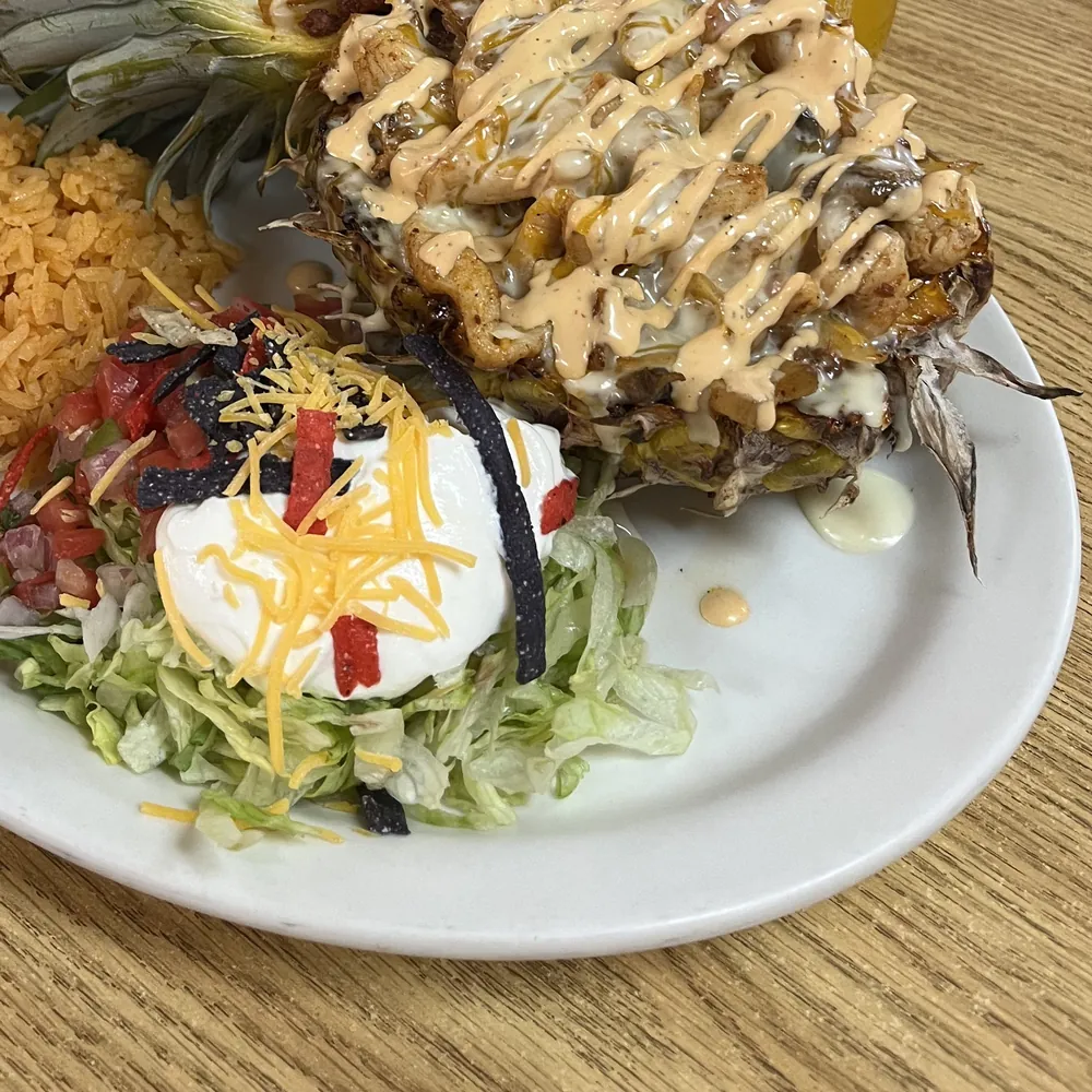 Lola's Pineapple: grilled chicken, chorizo and cheese sauce served in a halved pineapple, with rice and salad