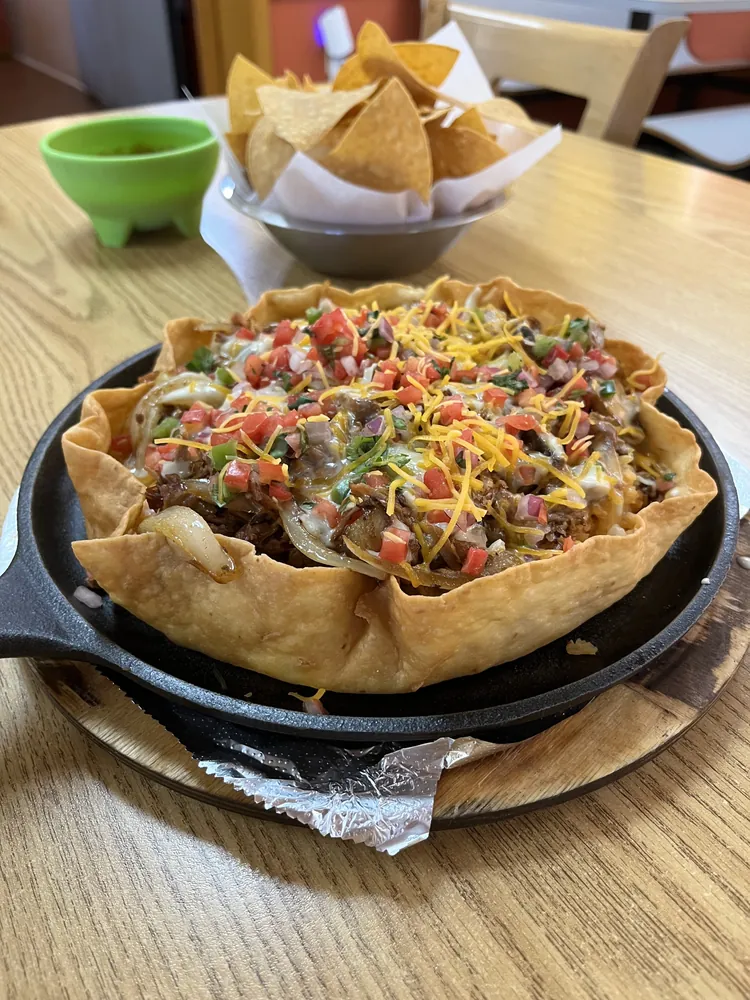 Volcán: crispy tortilla bowl on a skillet, filled with carnitas and topped with cheese and pico de gallo