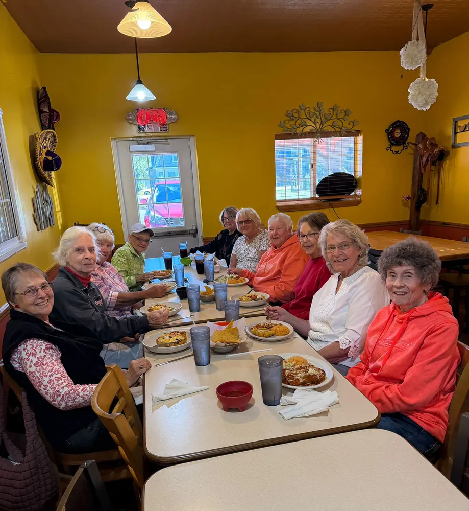 A group of friends smiling around a long table at Lola's with plates of food